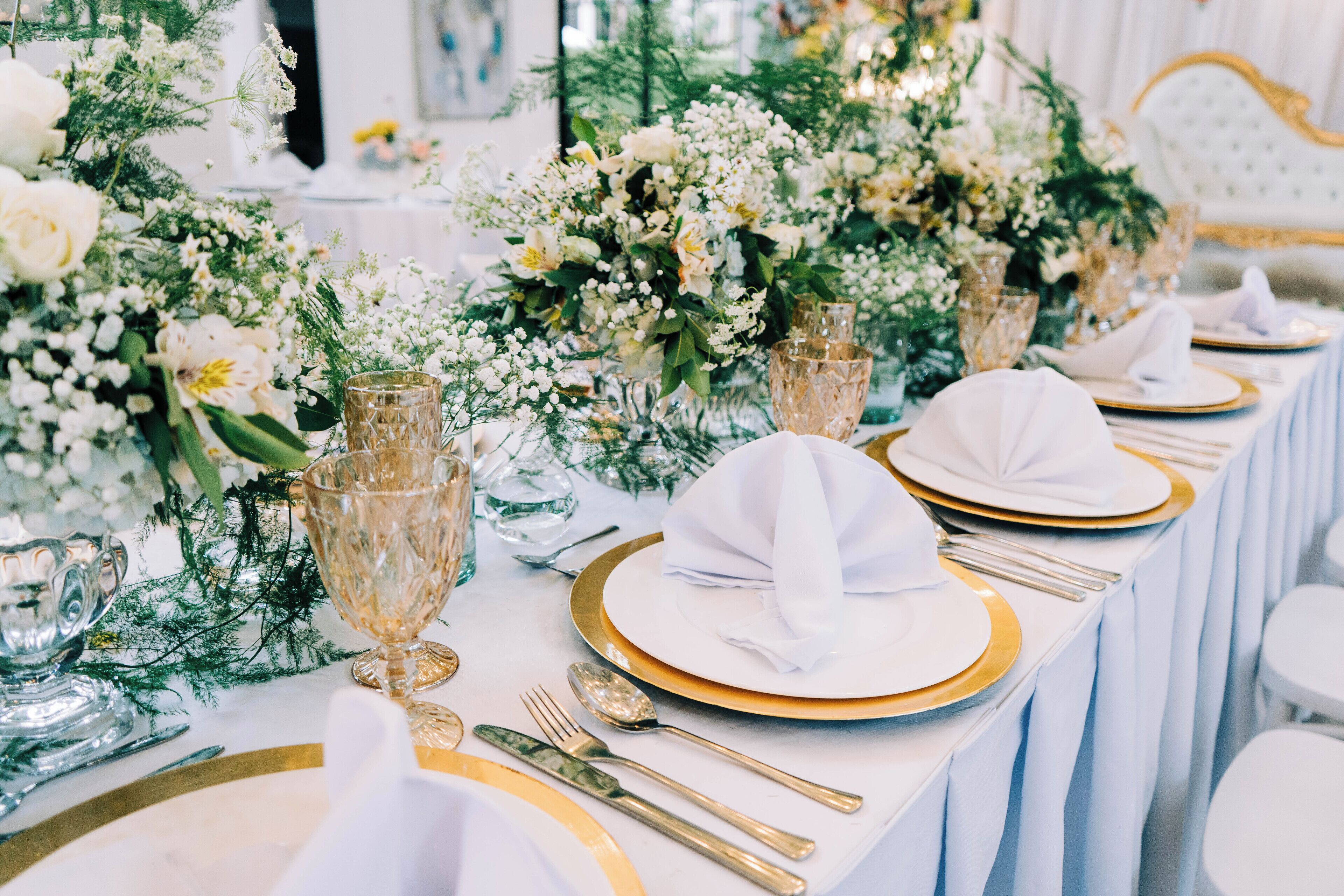 A table set with white napkins, gold and white plates, and clear glass goblets.