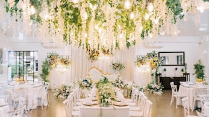 Een feestzaal voor een bruiloft, met witte tafels, stoelen en bloemendecoraties.