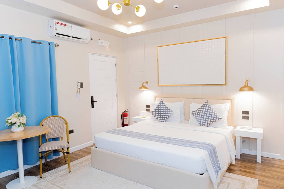 Ein Hotelzimmer mit einem Bett, Nachttischen, einem Sessel, einem kleinen Tisch mit einer Vase und einem blauen Vorhang.
