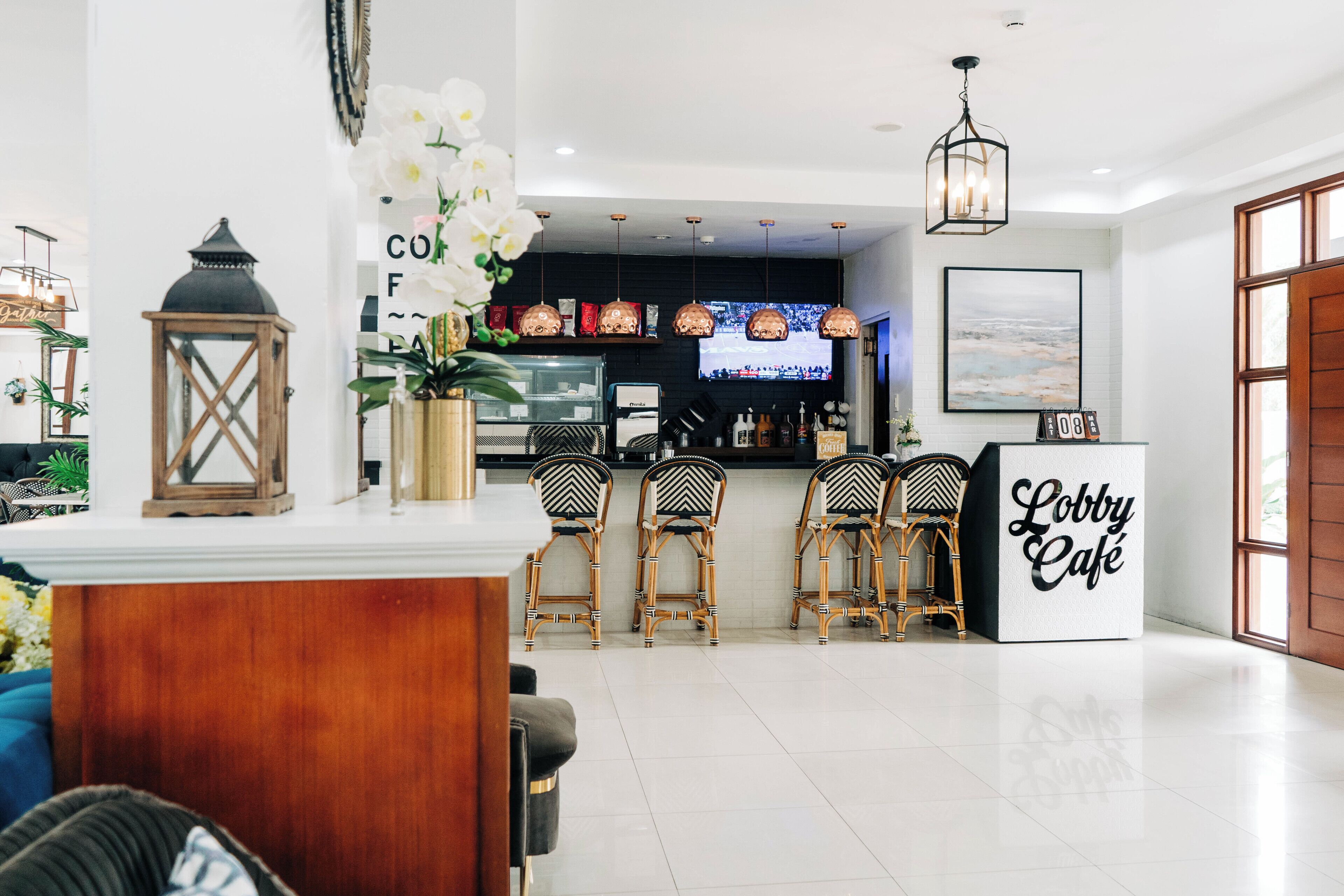 A lobby with a reception desk, wicker chairs, a coffee bar, and a sign reading "Lobby Café".