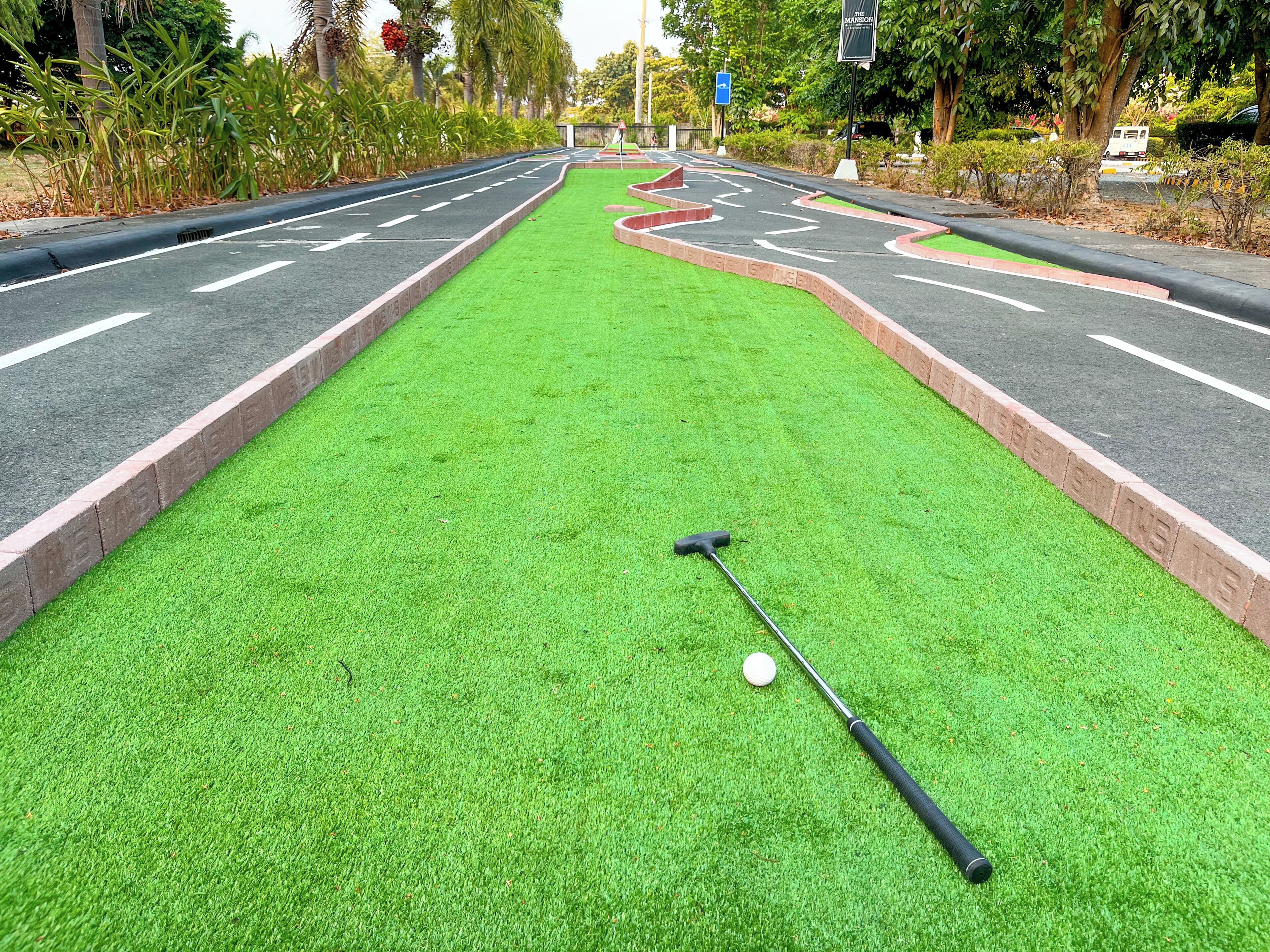 Ein Minigolfplatz mit grüner Spieloberfläche, einem Golfball und einem Schläger.
