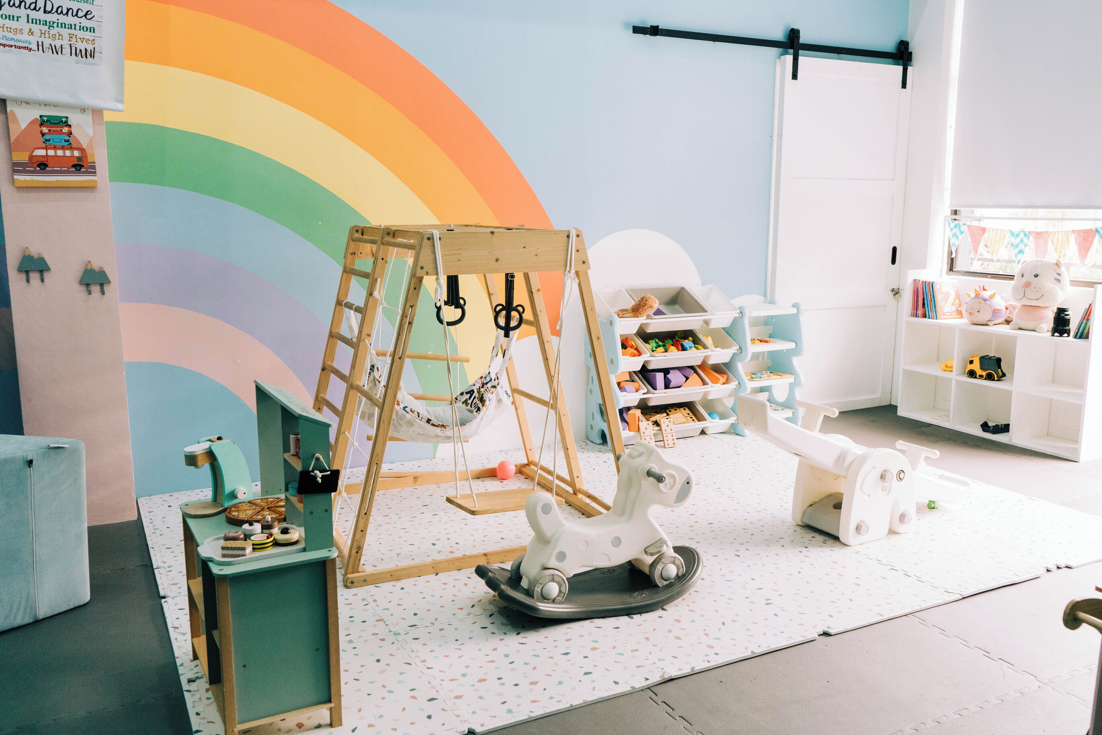 A playroom with a wooden swing set, a rocking horse, and a colorful wall mural.