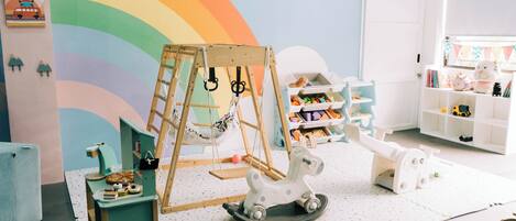 A playroom with a wooden swing set, a rocking horse, and a colorful wall mural.