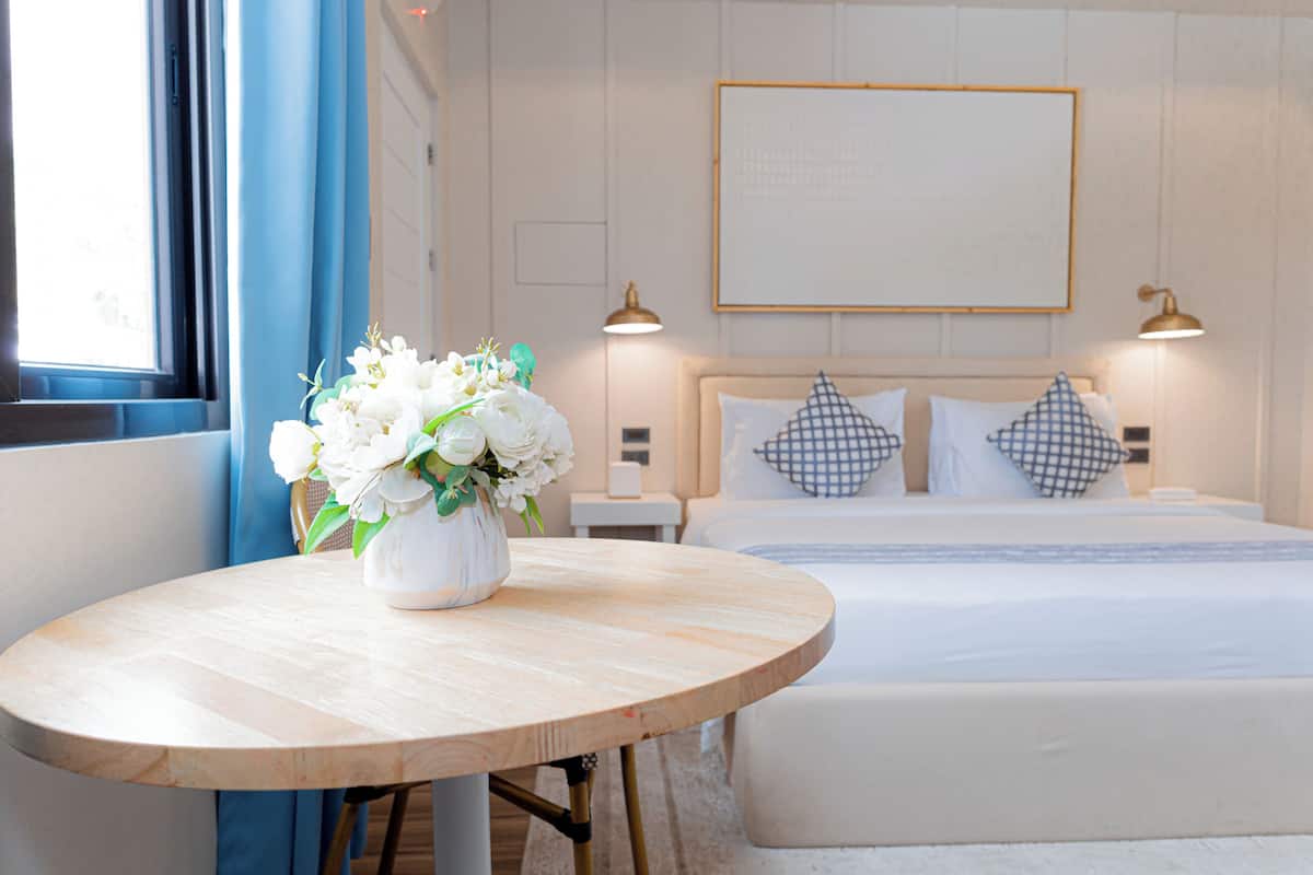 Ein Hotelzimmer mit einem Bett, einem runden Holztisch mit Blumenvase und zwei Nachttischlampen.