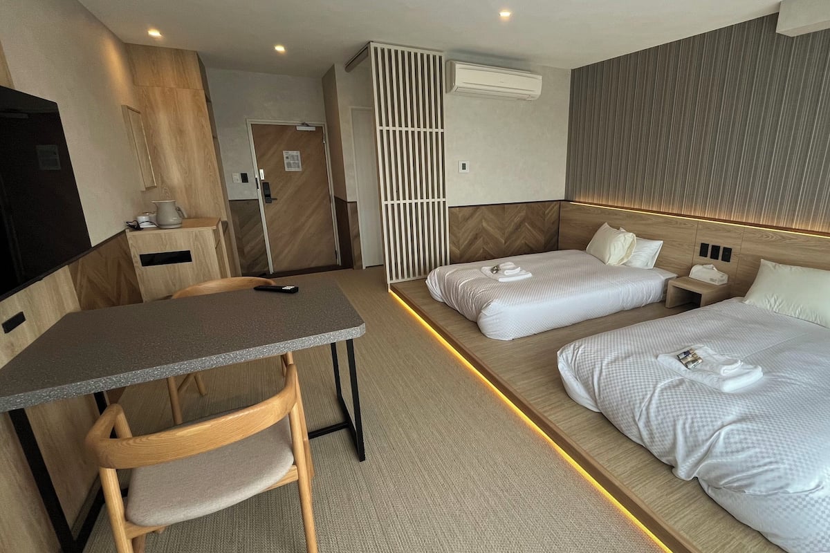 Habitación de hotel con dos camas, un escritorio, una silla, un aire acondicionado y un televisor.