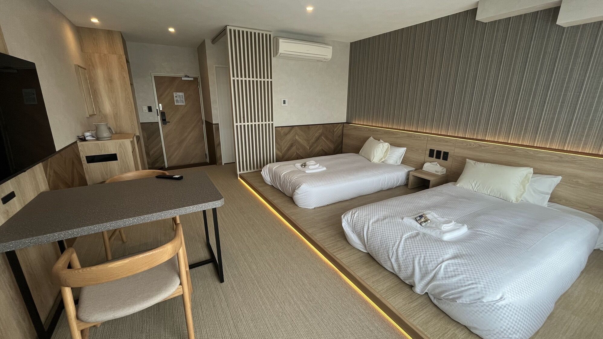 Een hotelkamer met een bureau, twee bedden, een televisie en een scheidingswand.
