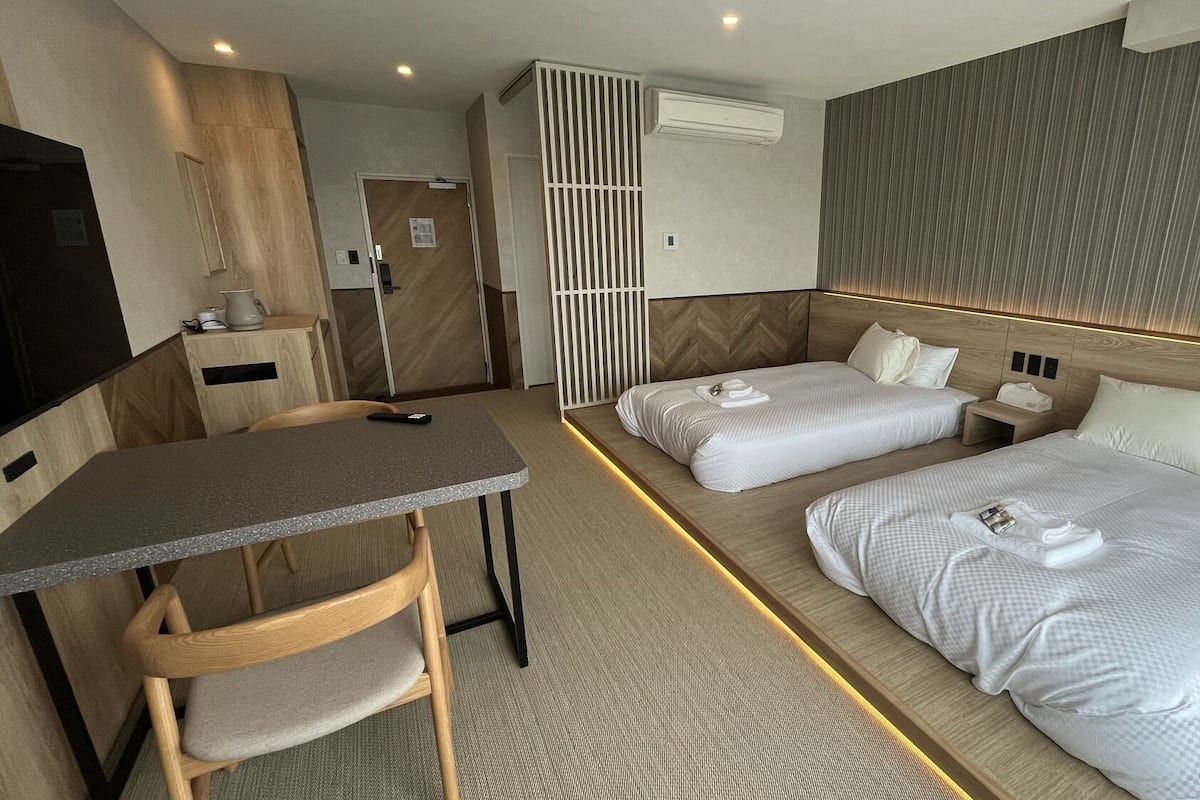 A hotel room with a desk, two beds, a TV, and a partition wall.