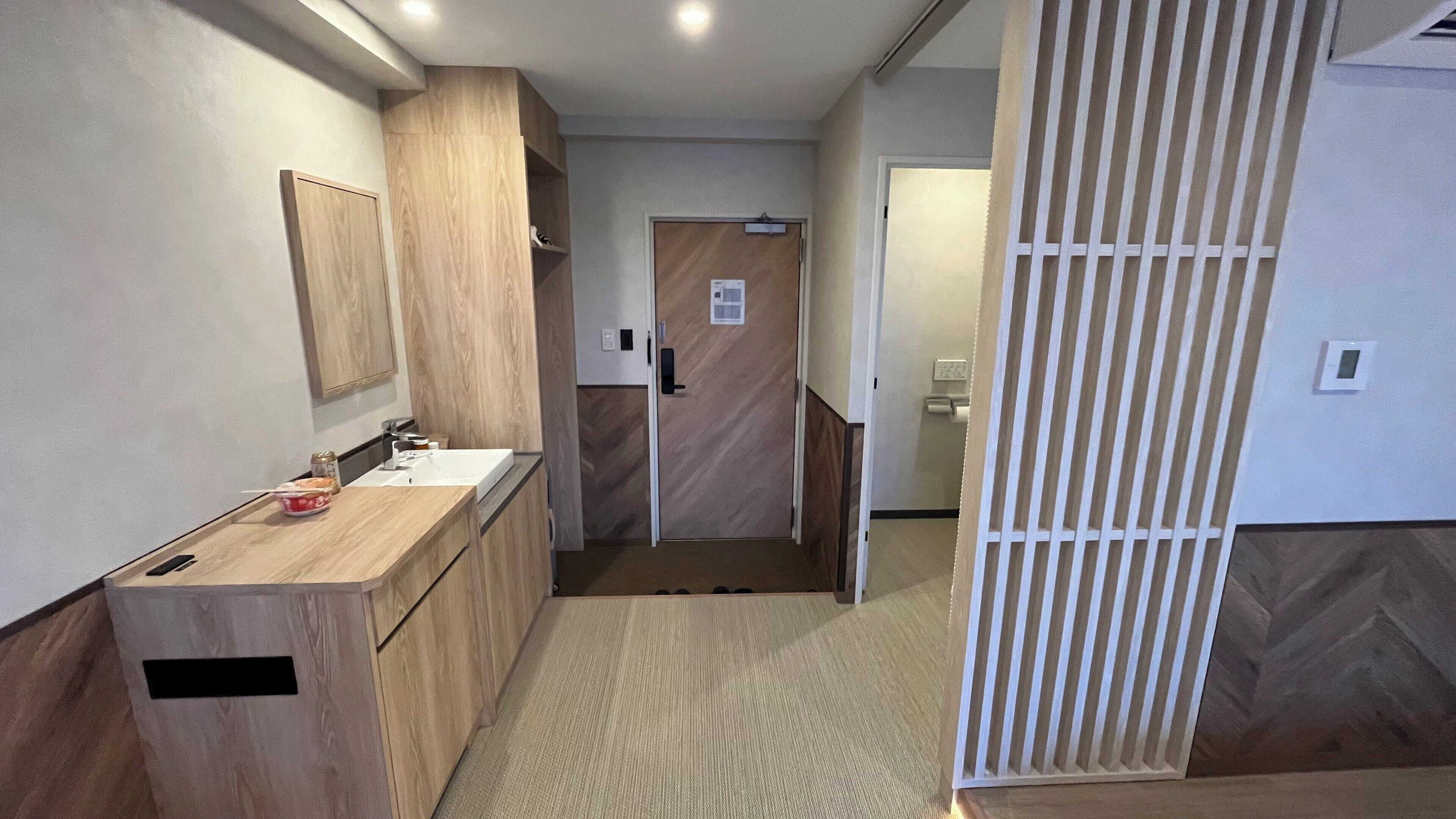 Une salle de bain moderne avec un meuble-lavabo en bois, un évier et un miroir. Une porte donne accès à une autre pièce.