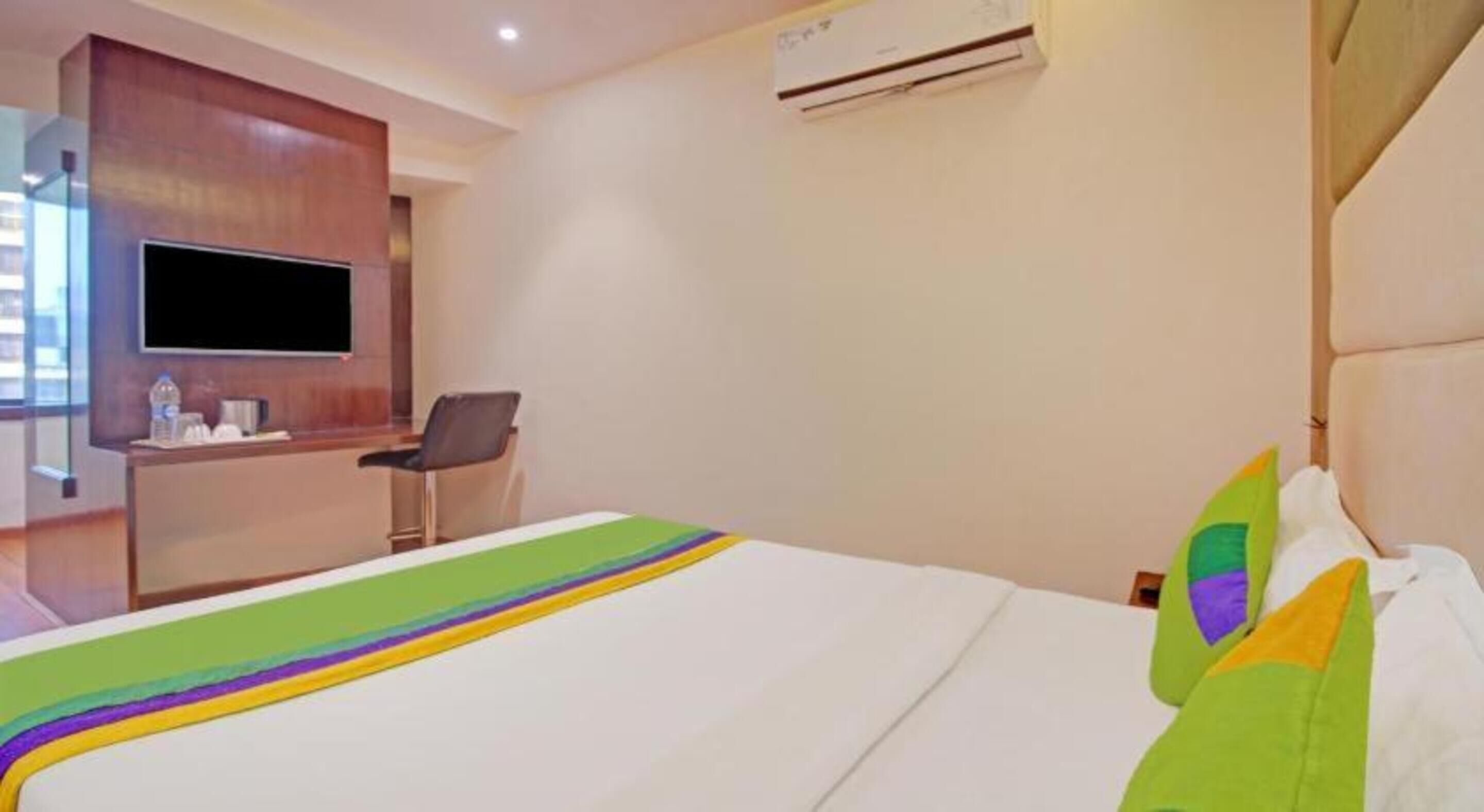 Ein Hotelzimmer mit Bett, Schreibtisch, Stuhl, Fernseher und Klimaanlage.