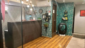 Un espace d’accueil comprenant un comptoir de réception en bois, une horloge murale, une plante en pot et un élément décoratif mural.