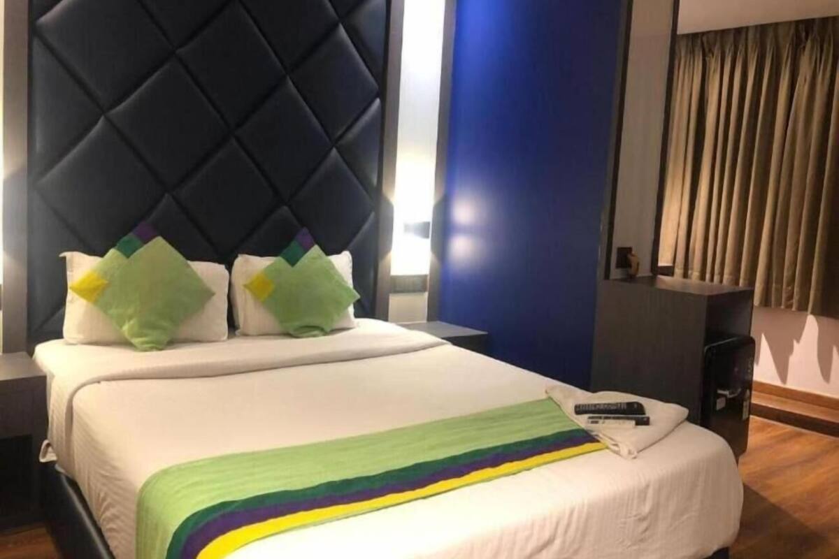 Ett hotellrum med en stor säng, en sänggavel, ett nattduksbord och ett fönster med gardiner.