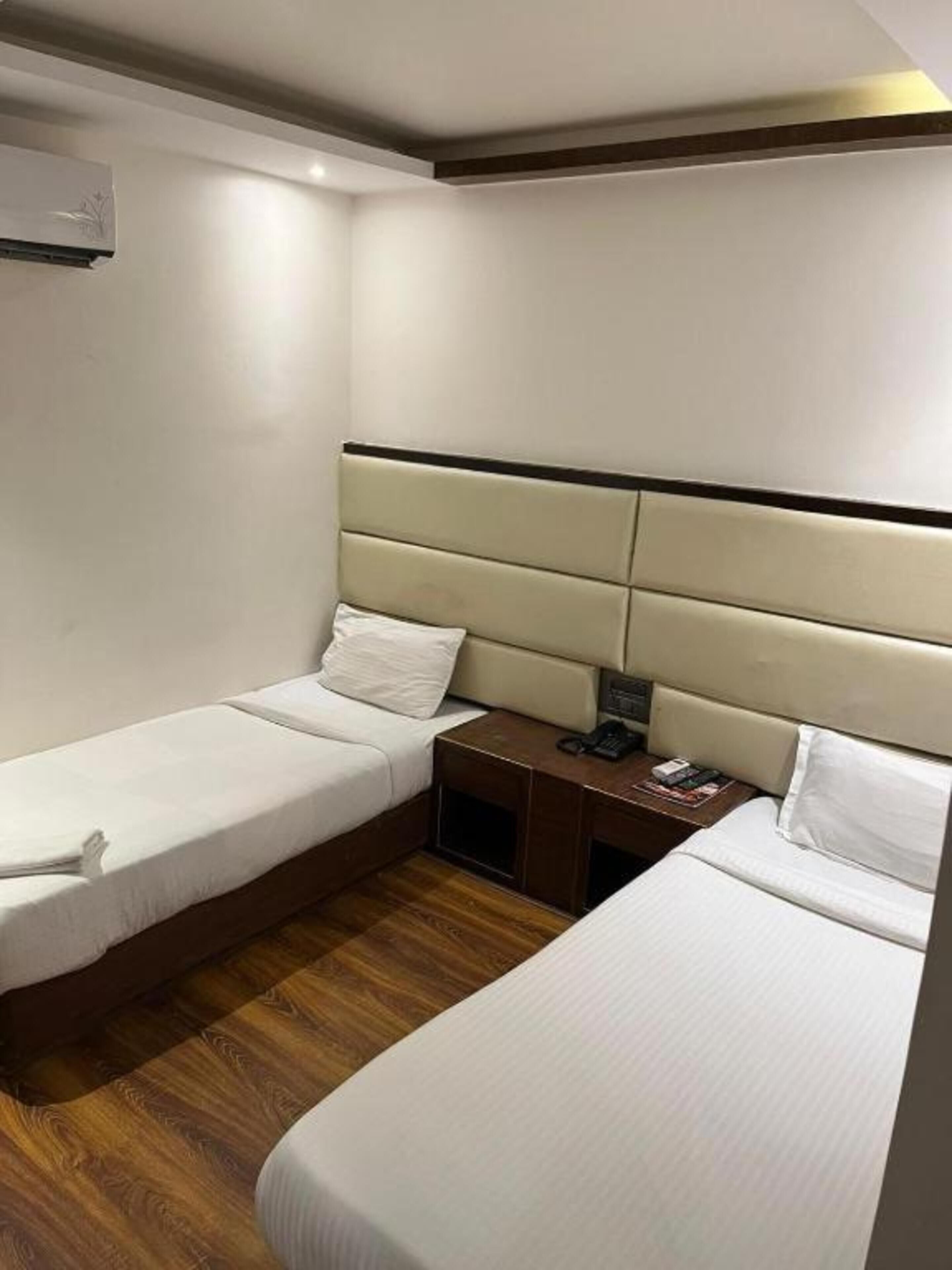 Habitación de hotel con dos camas individuales, piso de madera, una mesita de noche con teléfono y aire acondicionado de pared.