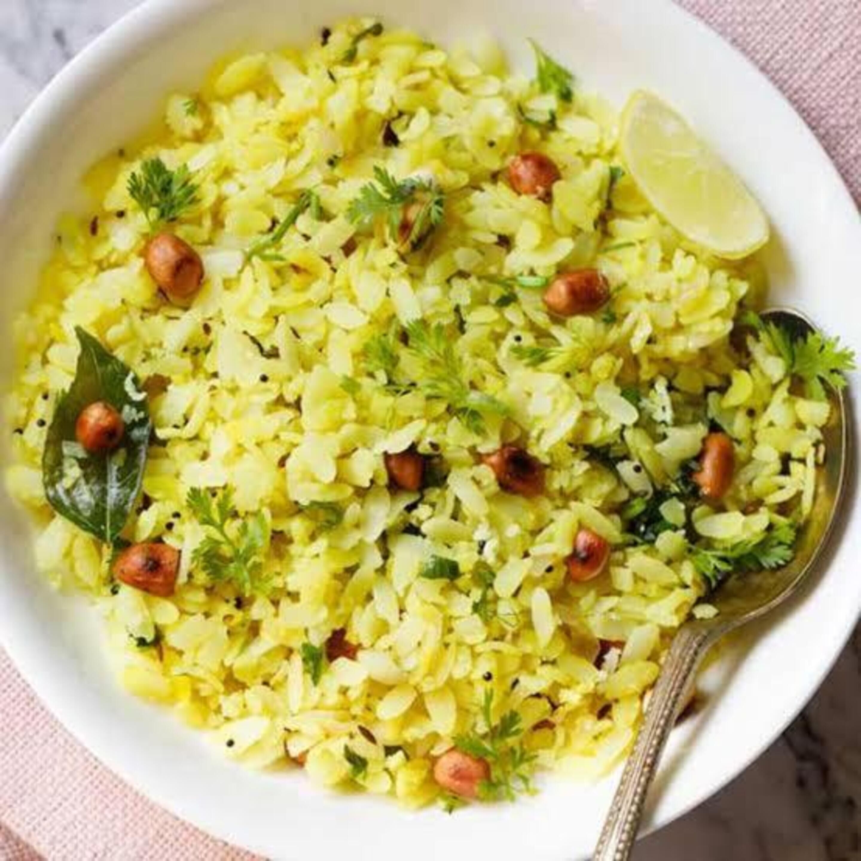 A bowl of yellow rice garnished with peanuts, cilantro, and a lime wedge.