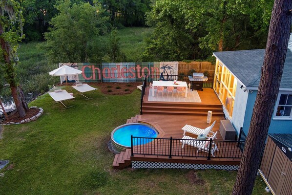 A backyard with a swimming pool, deck chairs, a barbecue area, and a sign reading "Charleston".