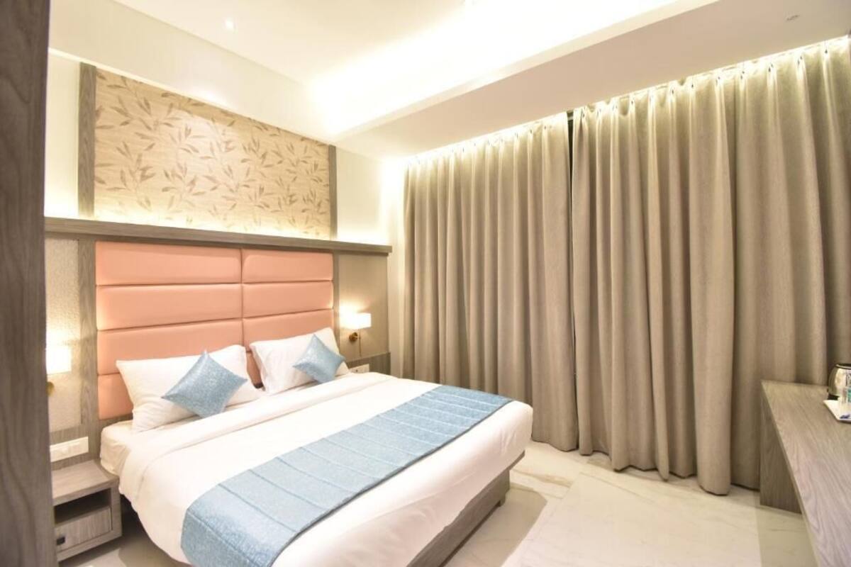 Una camera d'albergo con un letto grande, una testiera decorata con un motivo a foglia, un comodino, una scrivania e una finestra con tende.