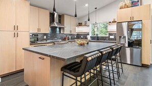 Una cucina moderna con isola centrale, sgabelli da bar, elettrodomestici in acciaio inossidabile e illuminazione a sospensione.