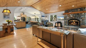 Un ampio soggiorno con camino in pietra, soffitto in legno e zona pranzo, con una cucina sullo sfondo.