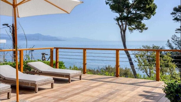 A wooden deck with lounge chairs and a canopy, overlooking a body of water and distant mountains.