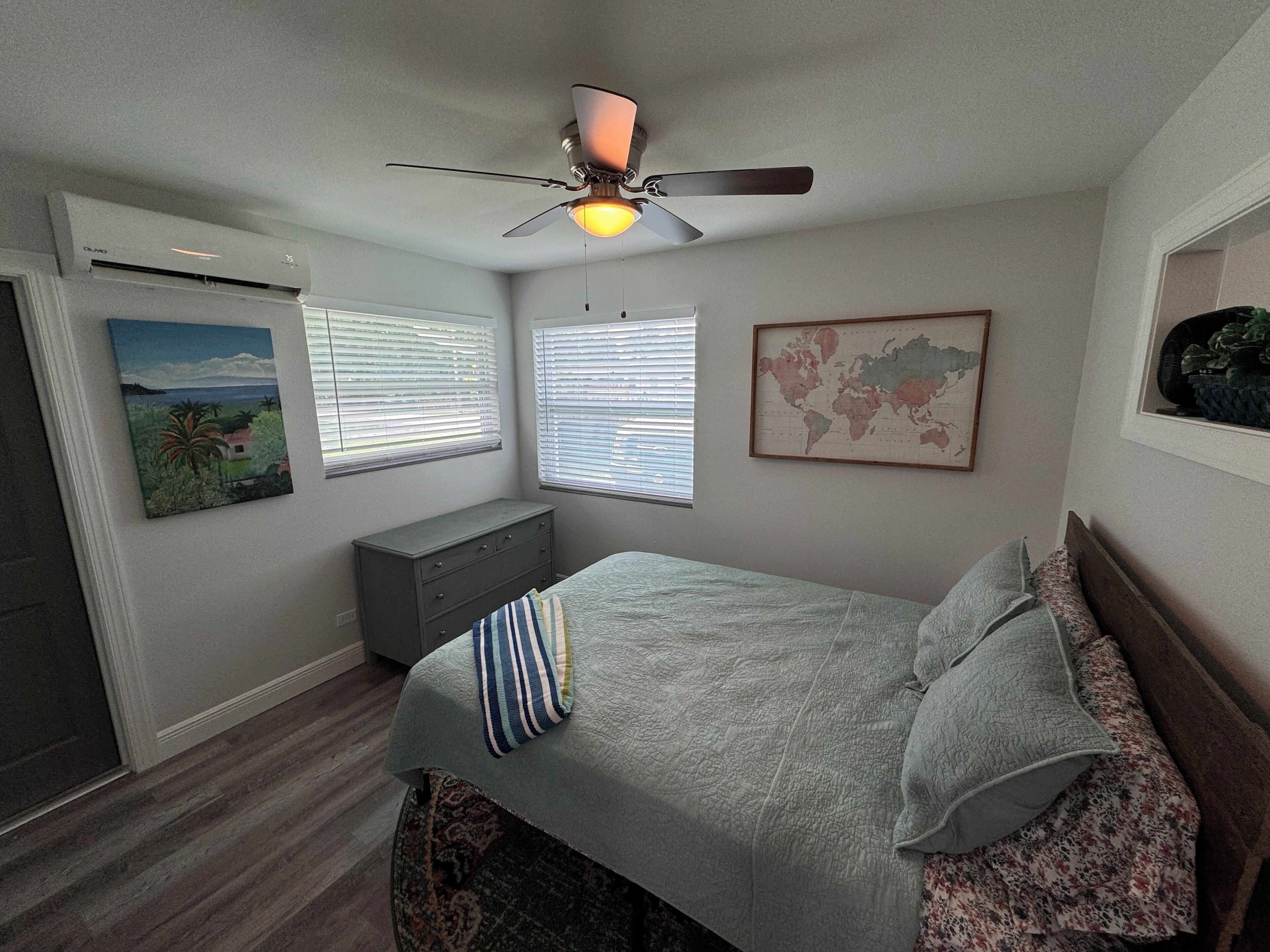 A bedroom with a bed, a dresser, a ceiling fan, and a world map on the wall.