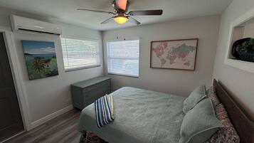 A bedroom with a bed, a dresser, a ceiling fan, and a world map on the wall.