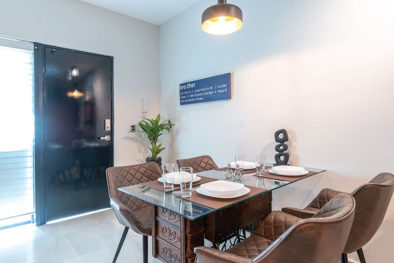 A dining area with a glass-top table, brown upholstered chairs, and a sign on the wall.