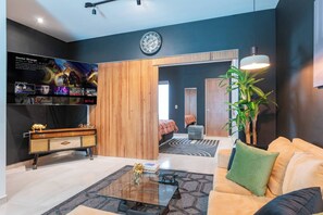 A modern living room with a flat-screen TV, a sofa, a coffee table, a wooden cabinet, and a large plant.