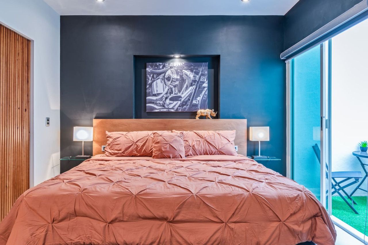A bedroom with a large bed, a headboard, a wall-mounted artwork, and a view through a sliding door.