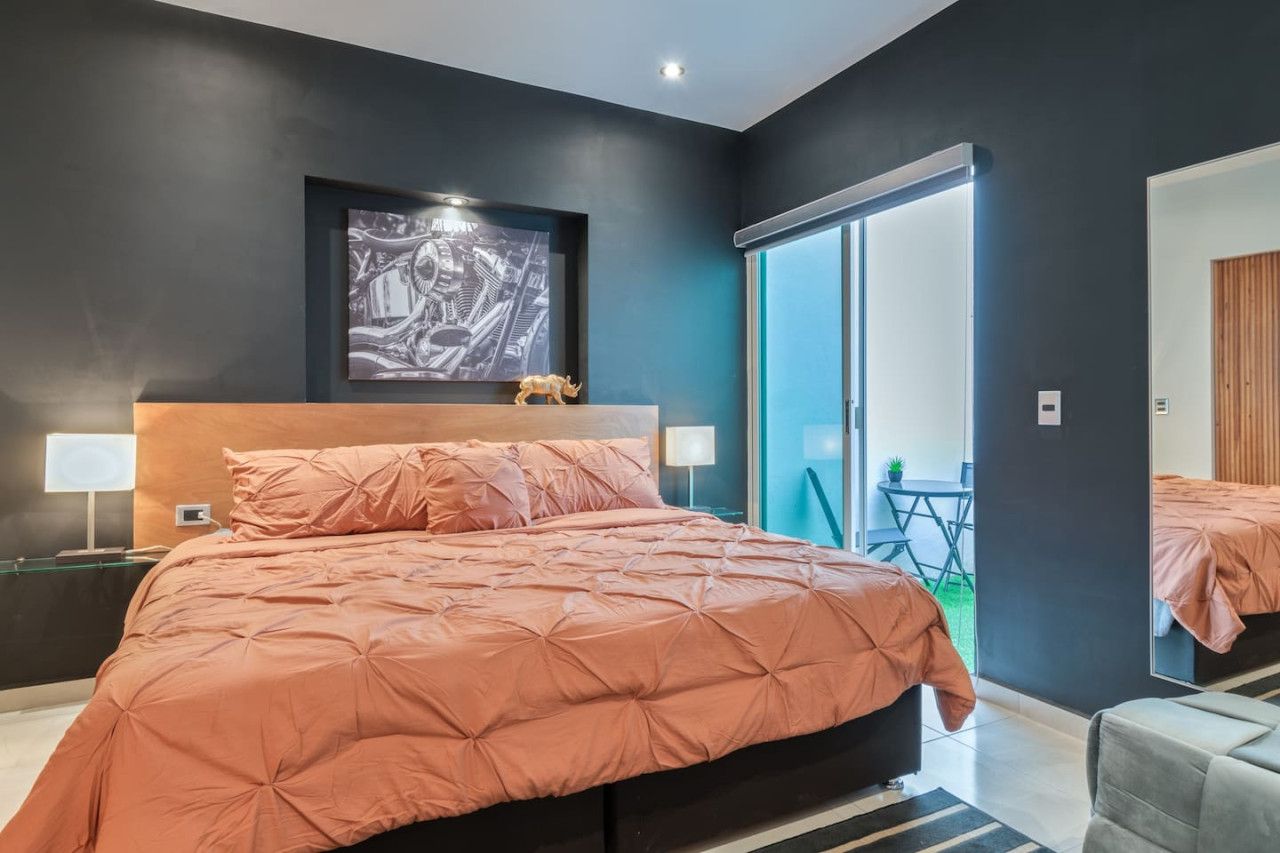 Quarto moderno com cama grande, cabeceira, obra de arte na parede e porta de vidro deslizante para uma varanda.