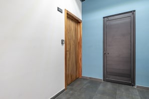 Um corredor com duas portas, uma de madeira e outra de metal, e uma placa com número acima da porta de madeira.