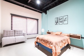 Quarto com cama, sofá, mesa de cabeceira e prateleira na parede.