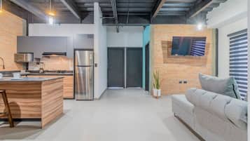 Una cucina moderna con isola integrata, elettrodomestici in acciaio inossidabile e un divano grigio in zona living.