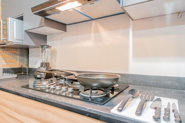 Cocina moderna con estufa a gas, licuadora y tabla de cortar con utensilios.