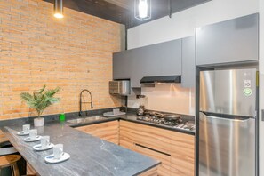 Een moderne keuken met een bakstenen muur, roestvrijstalen apparatuur en een zwart aanrecht.