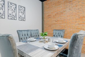Un comedor con pared de ladrillo, sillas tapizadas en gris, una mesa de madera dispuesta para cuatro comensales y decoración en la pared.