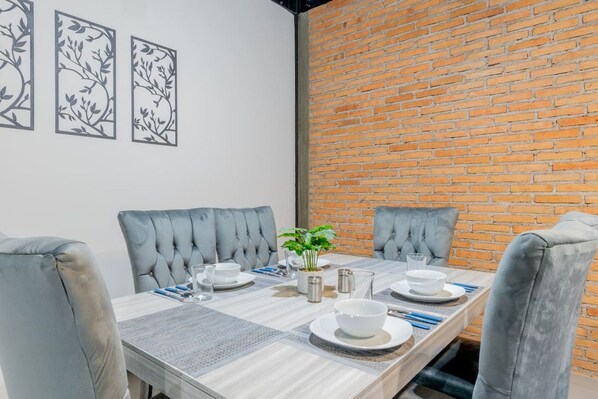 A dining area with a brick wall, grey upholstered chairs, a wooden table set for four, and wall art.