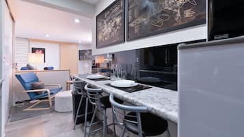 A modern kitchen with a marble countertop, bar stools, and a refrigerator.