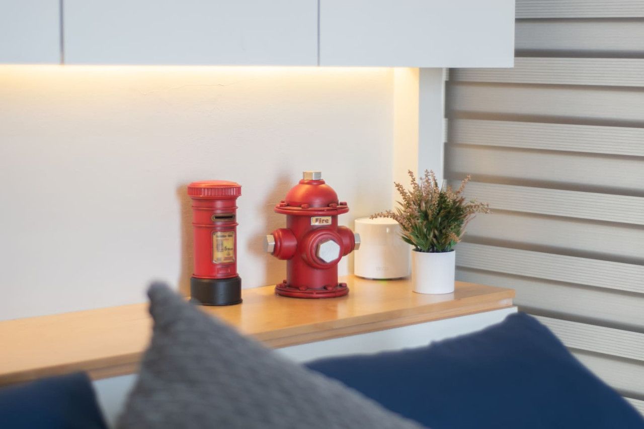 Une borne d’incendie rouge et une bouteille d’eau sont posées sur une étagère en bois, contre un mur recouvert de panneaux horizontaux.
