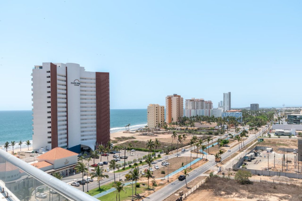A coastal cityscape with high-rise buildings, a beach, and a clear sky.