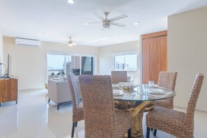 A dining area with a glass table, woven chairs, ceiling fans, and large windows with a city view.