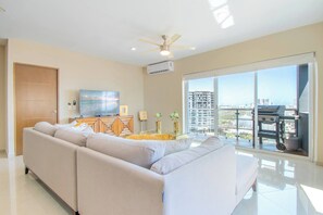 A modern living room with a sofa, TV, and a balcony with a city view.