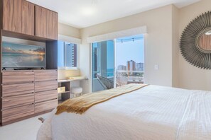 A bedroom with a bed, a TV, a desk, a chair, a balcony with a view, and a decorative mirror.