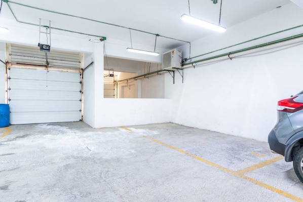 Un estacionamiento con piso de concreto, una puerta cerrada y un automóvil estacionado.