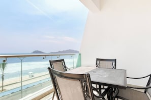 A balcony with a table and chairs, overlooking a beach and ocean.