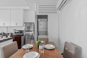 Una cocina moderna con zona de comedor, que incluye un refrigerador, horno, microondas y una mesa de comedor dispuesta con platos y vasos.