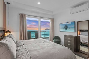 Une chambre d’hôtel avec un grand lit, un bureau, une chaise, une commode et une vue sur l’océan.