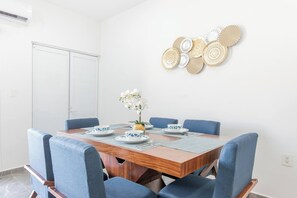 Un coin repas avec une table en bois, des chaises à l’assise rembourrée de couleur bleue, des œuvres d’art décoratives accrochées au mur et un ananas en guise de centre de table.