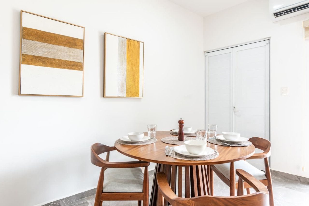 A dining area with a round wooden table, four chairs, and two framed artworks on the wall.
