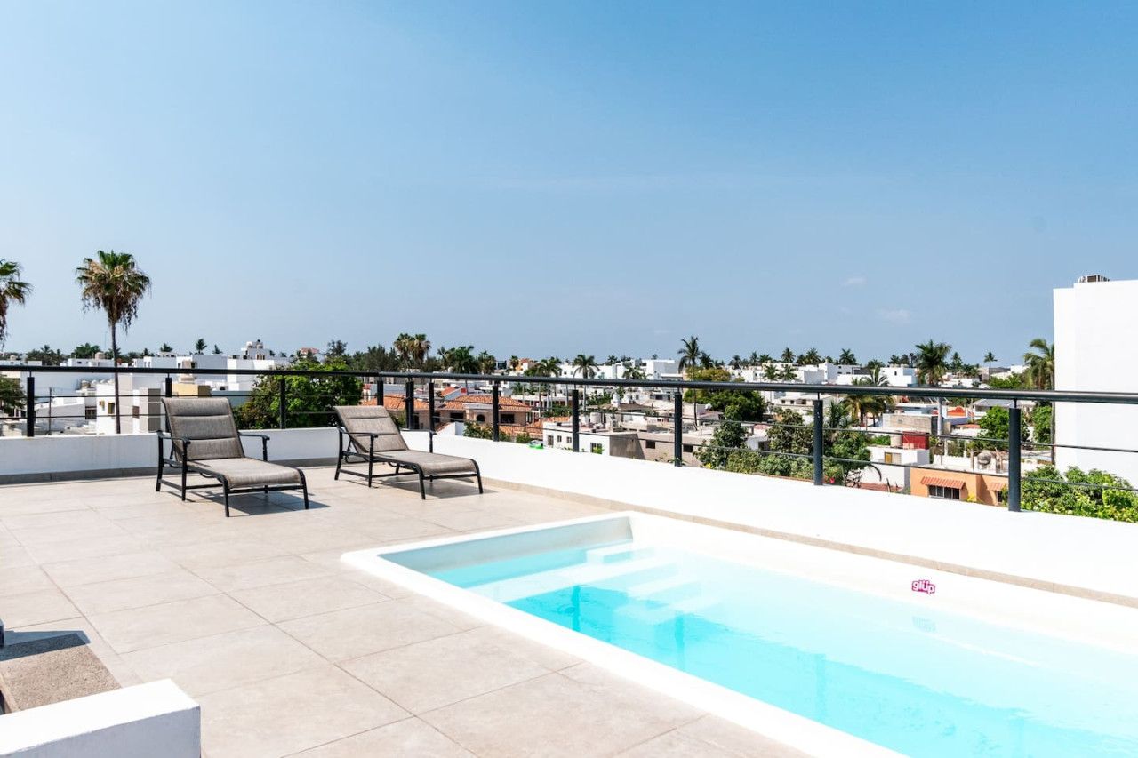 Ein Poolbereich auf dem Dach mit Liegestühlen und freiem Blick auf die Stadtlandschaft.