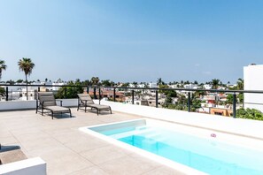 A rooftop pool area with lounge chairs and a clear view of the cityscape.