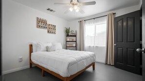Een slaapkamer met een bed, een plafondventilator, een raam met gordijnen en een deur.